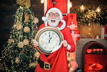 圣诞老人拿着时钟与圣诞节倒计时或新年圣诞老人在木制家庭内部显示时钟上的时间图片