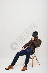 有本书的时尚男子坐在椅子上 与白种背景隔绝图片
