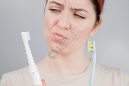 幸福的女人将牙刷与电动牙刷进行比较 女孩选择口腔卫生用品图片