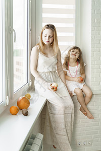两个穿白裙子的女孩坐在一个白色厨房的窗边吃着水果 却坐在窗户边图片