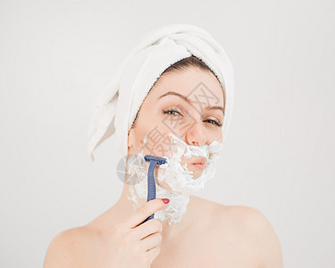 可爱的女人 头上戴毛巾 脸上有剃须泡沫 在白色背景上拿着剃刀身体沙龙头发胡子工作室浴室护理卫生治疗快乐图片