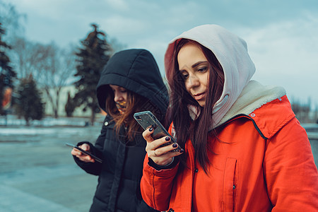 近距离的年轻女性在城市公园里浏览智能手机 使用手机戴兜帽的漂亮女性社交网络闲暇依赖会议天气朋友们寒冷娱乐社交兜帽图片