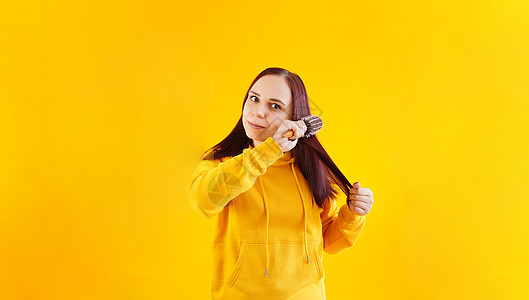 年轻女人用黄色背景梳理头发的肖像 在看相机时 黄帽饰上涂着黑发女性闲暇水平工作室梳子外貌表情配饰个性性格图片