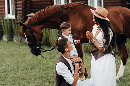 白衣家庭与儿子一起站在两匹美丽的自然马旁 一对有孩子的时装夫妇被用马拍下照片 a 一名男子童年男生自由妈妈衣服男人帽子农场动物幸图片