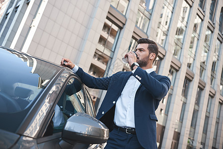 有自信的商务人士在街上站在汽车旁边喝咖啡 却又站着一辆车旁图片