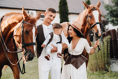 白衣家庭与儿子一起站在两匹美丽的自然马旁 一对有孩子的时装夫妇被用马拍下照片 a 一名男子牧场母亲衣服农场农村动物父亲童年马术牛图片