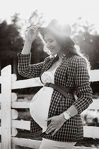 身戴大肚皮的怀孕女孩 在日落时在马圈附近戴着帽子 穿着棕色洋装和马匹的年轻孕妇脚垫母性动物父母生活奇迹幸福生育力家庭肚子图片