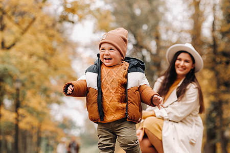 母亲和儿子在秋天的公园散步 一家人在金色的秋天穿过自然公园季节幸福白帽母性孩子婴儿妈妈大衣假期叶子图片