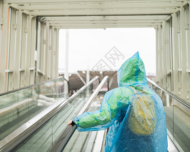 穿雨衣的女人在扶梯上升起 身着保护服的女孩从雨中出来 背视图片