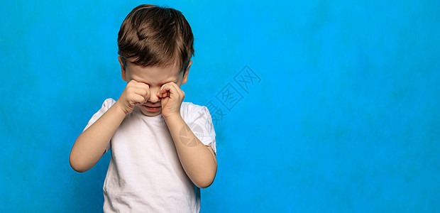 一个蓝色背景的男孩揉了揉眼睛 眼睛健康 眼睛疾病 一个爱哭的婴儿 儿童疲劳 心理学眼泪黑色疼痛哭泣男生童年孩子图片