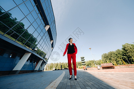 一个穿红色西装的女孩站在城市现代建筑的背景下套装玻璃商业奢华魅力街道女士外貌黑发裤子图片