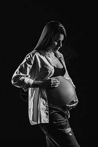 在黑背景工作室穿白衬衫和牛仔裤的怀孕妇女大肚子母性成人孩子衬衫母亲肚子腹部诞生女孩图片