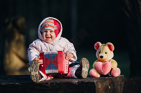 有趣可爱的女孩 一个穿着时髦牛仔裤的小孩拉手风琴 快乐宝贝玩游戏 可爱的萌娃 一个微笑的婴儿的美丽而富有表现力的笑声图片