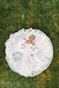 一位穿着白色婚纱躺在地上的美丽新娘的肖像 绿草上一位优雅新娘的照片 新娘的顶级照片黑发工作室皮肤女士庆典耳环奢华幸福魅力冒充图片