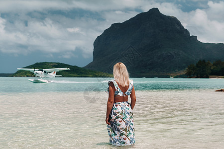 一个穿着泳衣的女孩站在海里 在毛里求斯岛的勒摩尔峰的背景下等待一架水上飞机 水中的一个女人回头看着一架降落在毛里求斯岛的飞机太阳图片