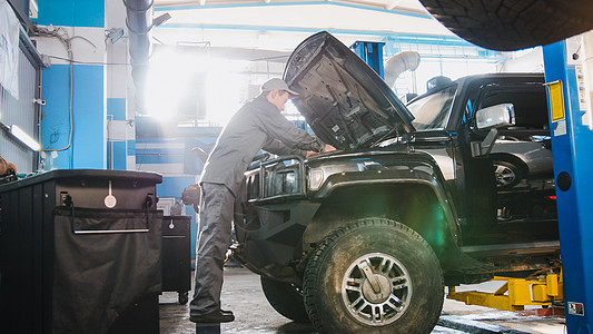 汽车车库的男性机械男子检查车头 寻找豪华SUV 宽角图片
