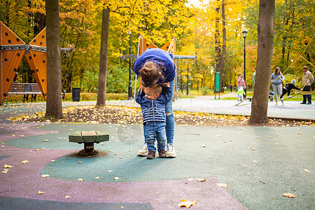 穿着蓝衣服的妈妈和小孩在秋天公园的操场玩乐 童年快乐概念图片