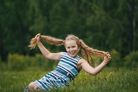 穿着蓝色夏装的微笑女女孩在公园里玩图片