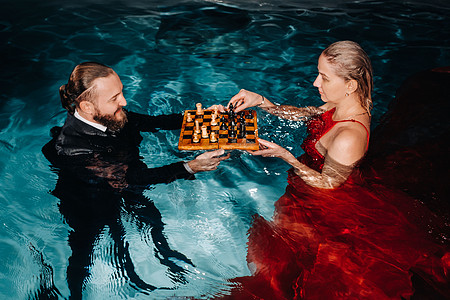 一个穿西装的男人和一个穿红裙子的女孩 在游泳池的水上下棋象棋玩家运动很多人思考红色棋手蓝色消遣礼服图片