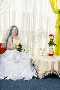 一位幸福的犹太新娘 她的脸上蒙着面纱 上面放着一束白玫瑰 坐在犹太教堂里 然后在一张放着鲜花的桌子上举行 Huppa 仪式图片
