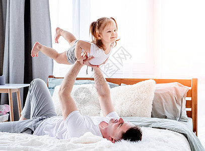 父亲和女儿在床上女性微笑孩子男人拥抱爸爸父母卧室说谎乐趣图片