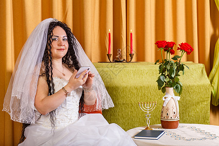 一名穿着白色婚纱 面纱的犹太新娘坐在桌子上 鲜花在教堂仪式前即时送信者中传来图片