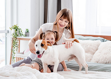 母亲与女儿和狗在床上快乐毯子乐趣卧室女士女孩父母说谎微笑拥抱图片