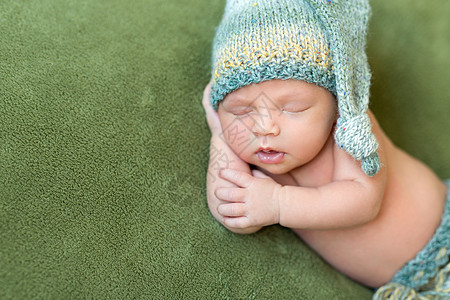 睡着张开嘴 穿着编织帽子的可笑婴儿新生姿势绿色说谎尿布生活休息身体毯子梦幻图片