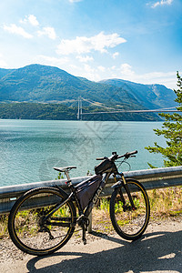 斯堪的纳维亚山地自行车运动的主题 挪威西南部悬索桥上戴着头盔和运动服的人类游客骑着自行车穿越挪威西南部的 Hardanger 峡图片