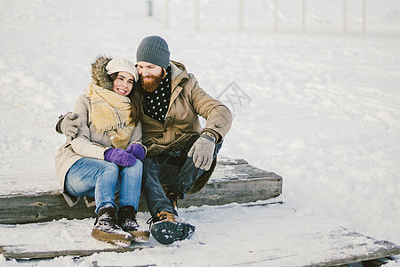 恩爱的年轻人一个留着胡子的男人和一个白人女人在冬天坐在木制楼梯上 在雪地上圣情人节约会圣诞节拥抱和快乐家庭女士海滩男朋友胡须幸福图片