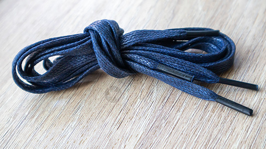 一张深蓝色的平板鞋带片子 上面有鞋子的细小提示 卷起来 在木制背景上被隔离花边单品蓝色纺织品蕾丝物品配饰绳索线圈自色图片
