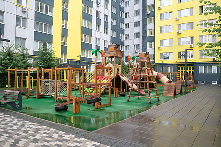 一个高层建筑的庭院 在一个没有人的雨天 有一个由木头和塑料制成的现代大型游乐场 空荡荡的户外游乐场 儿童游戏和运动的场所民众娱乐图片