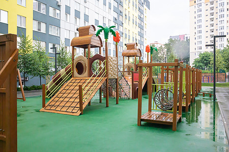 一个高层建筑的庭院 在一个没有人的雨天 有一个由木头和塑料制成的现代大型游乐场 空荡荡的户外游乐场 儿童游戏和运动的场所活动地面图片