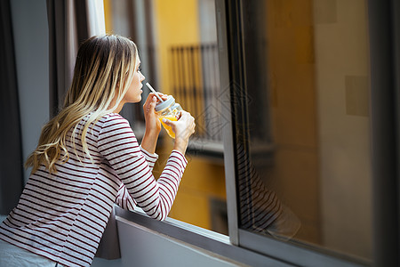 年轻女子喝着一杯天然橙汁 从家窗外倾斜而下 从家里走出来果汁食物水果头发成人快乐女孩黑发女性玻璃图片