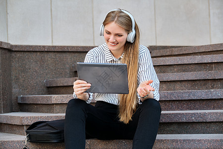 坐在城市台阶上坐着的持数字平板电脑耳机的年轻美女太阳成人微笑活动技术金发女郎视频学生幸福互联网图片