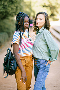 两名多族裔妇女在街上一起看照相机 在街上看着镜头黑发城市学生快乐辫子黑色发型女性乐趣女孩图片