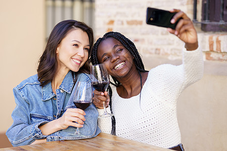 两个女人用智能手机拍自拍 喝杯酒 然后喝酒假期快乐朋友女性微笑乐趣玻璃酒吧辫子幸福图片