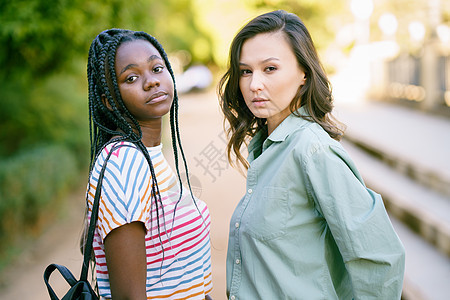 两名多族裔妇女在街上一起看照相机 在街上看着镜头女孩衣服友谊女性喜悦城市快乐黑色头发爆炸图片