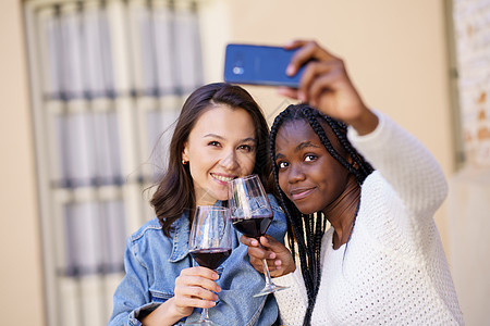 两个女人用智能手机拍自拍 喝杯酒 然后喝酒两个人微笑女性幸福假期游客辫子头发黑发乐趣图片