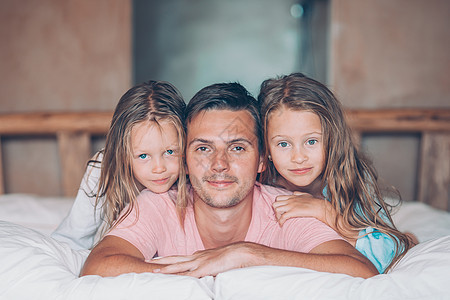 父亲和两个可爱的小女孩 在床上笑着玩得开心孩子男性说谎卧室母亲感情拥抱家庭孩子们男人图片