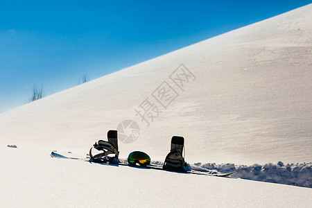 滑雪板和滑雪谷歌 在自由斜坡附近的雪上躺下风镜旅游太阳单板假期粉末活动天气高山蓝色图片