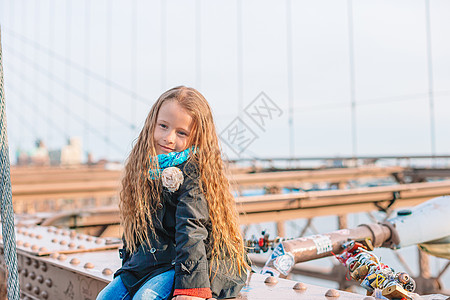 坐在纽约布鲁克林大桥的可爱的小姑娘们观光吸引力地标享受日落旅游建筑学女士旅行孩子背景