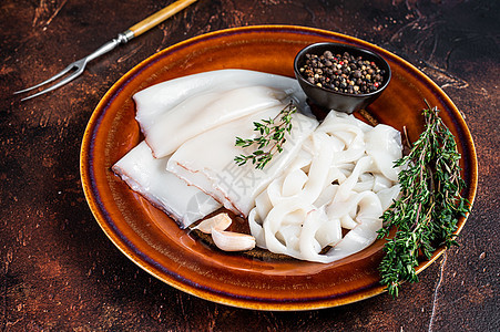 切片生环状鱿鱼 在一个有迷迭香的锈盘子里 深色背景白色厨房胡椒黑色海鲜木板管子戒指烹饪食物图片