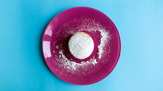 在粉红色的盘子上 在蓝色背景中 在顶部视图中撒上一块带糖粉的奶酪 甜点 一个小纸杯蛋糕 食物的概念 质地轻盈的白色烤饼干 复制空图片