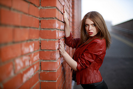 在红砖墙附近 身穿黑色拖链和红色皮夹克的年轻女子肖像女郎潮人牛仔裤女士城市女孩女性金发街道衬衫图片