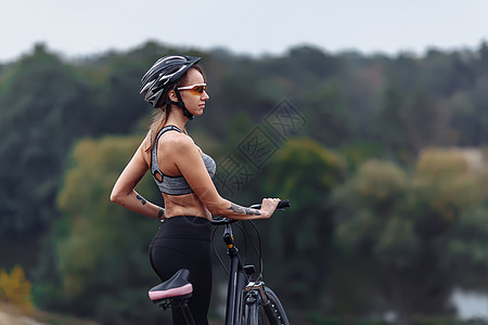 身穿运动服 穿着自行车站在岩石背景的脚踏车边站着的漂亮年轻女子运动衣服休息森林训练闲暇娱乐冒险运动装女孩图片