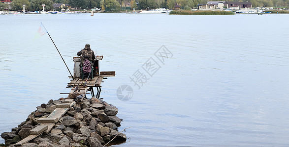 一位渔夫在河里捕鱼 后视 从河岸 一位渔民坐在河岸的木石桥上捕鱼 运动 休闲 生活方式木板日落海滩风景鹅卵石天空海岸钓竿娱乐寂寞图片