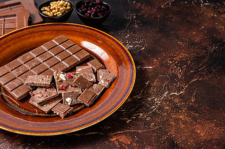 土制牛奶巧克力 配有栗子 花生 红莓和冻干草莓 放在锈盘上 深色背景 顶部视图 复制空间图片