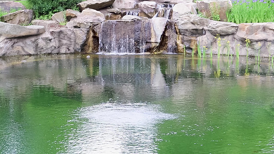 一个装饰性的小瀑布溅入池塘 在公园或花园中使用石头和水进行景观美化 雨林中的自然景观图片