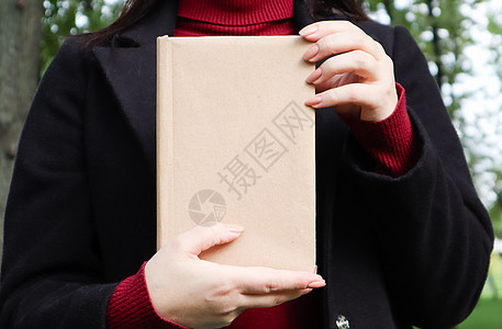 在公园里 穿着黑色羊毛大衣和勃艮第毛衣的女人拿着一本空封面的书的特写镜头 您的书籍阅读概念背景布局的自由空间文学学生女孩女性图书图片